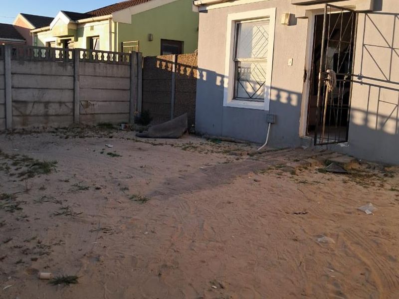 Rear exterior view of a house featuring a sandy yard, precast concrete boundary wall, and a security gate at the entrance.