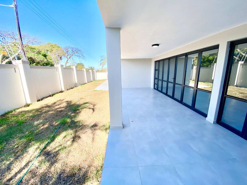 A spacious covered patio featuring modern tiled flooring and large glass sliding doors, overlooking a private garden area with a perimeter wall.
