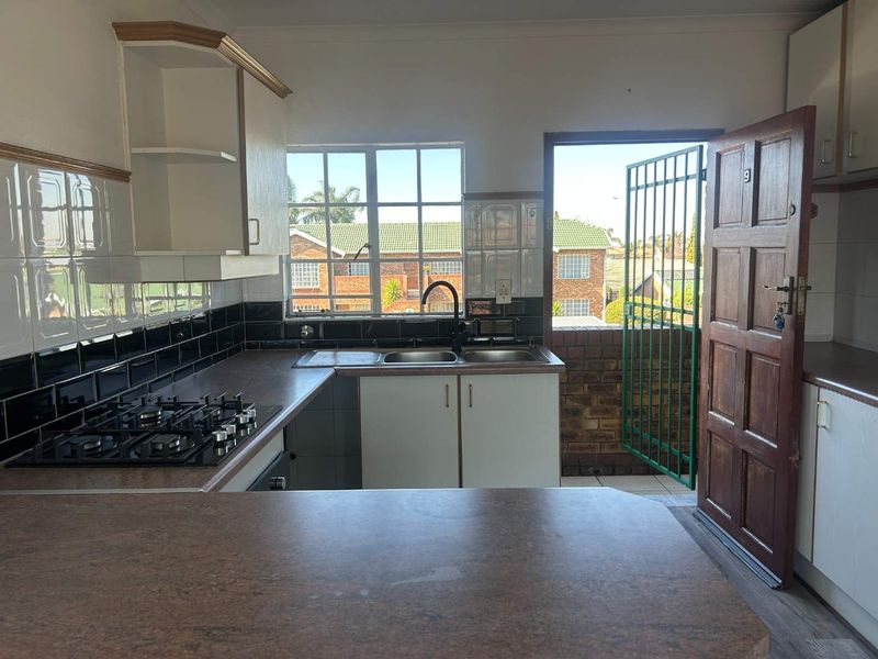A functional kitchen featuring a gas hob, built-in oven, double sink, and direct access to an outdoor area through a security gate.