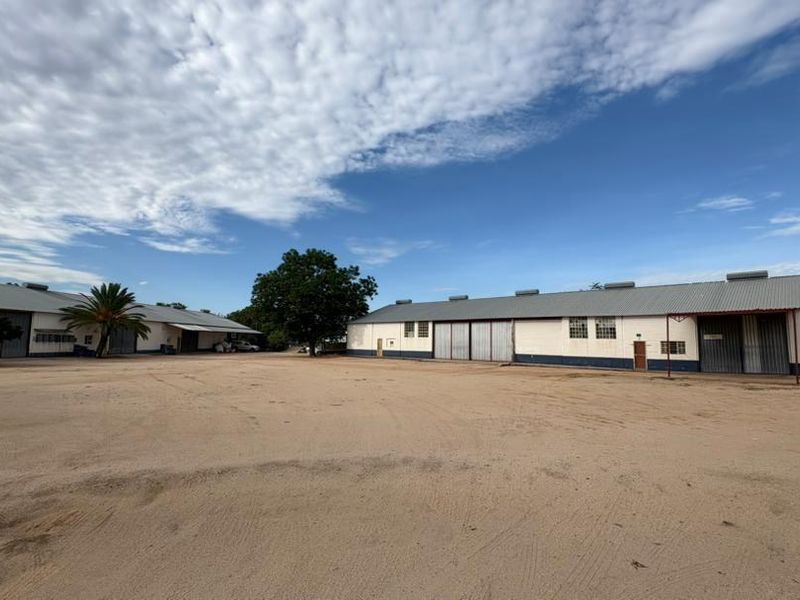 Wide angle view of a commercial property featuring multiple industrial warehouse buildings with large sliding doors and a spacious unpaved yard area.