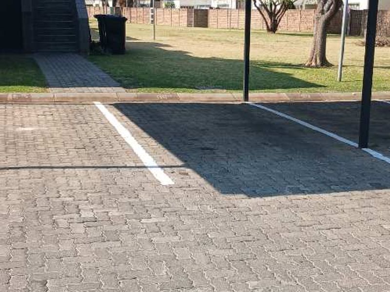 A covered carport parking bay with paved surfacing, situated within a residential apartment complex.