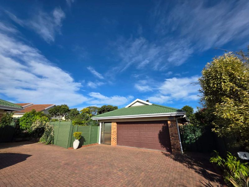 Front view of the townhouse featuring a brick driveway, double garage, and well-maintained green tiled roof with perimeter fencing.
