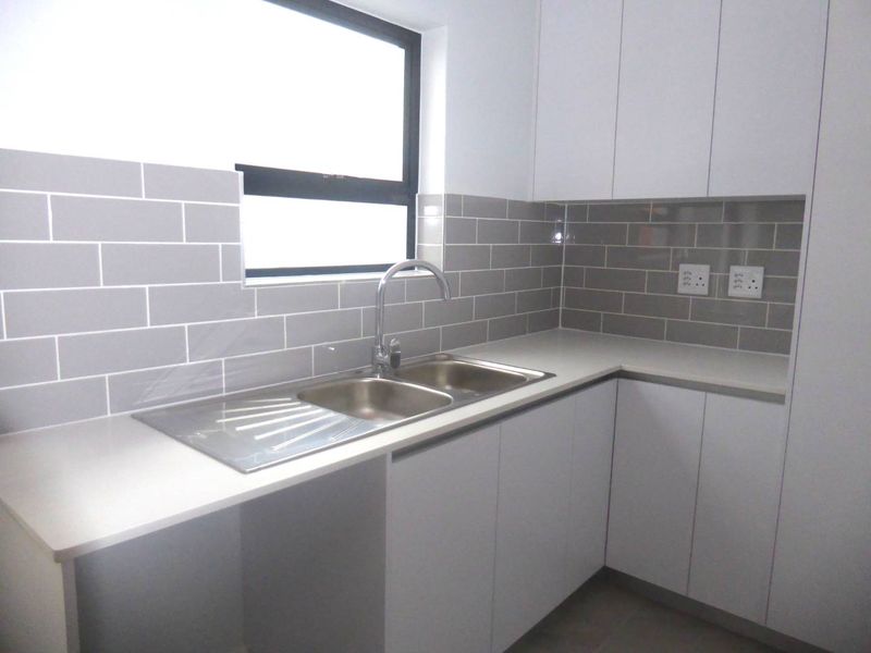 A modern, clean kitchen featuring white cabinetry, stone countertops, a stainless steel sink, and a stylish grey subway tile backsplash.