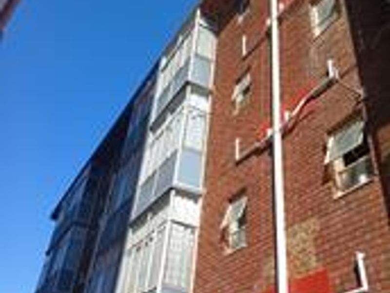A low-angle view of the apartment building's rear brick facade featuring exposed external plumbing and multiple casement windows.