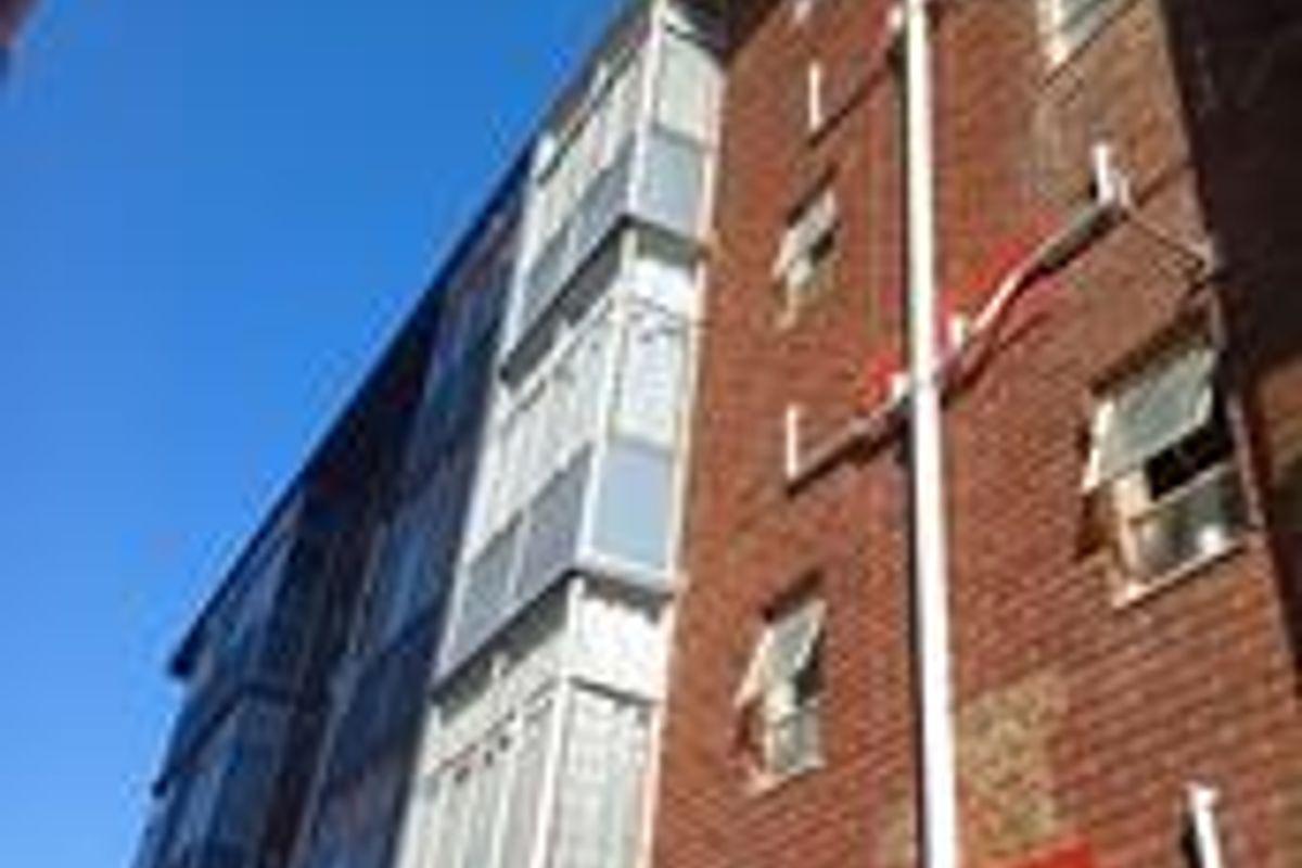 A low-angle view of the apartment building's rear brick facade featuring exposed external plumbing and multiple casement windows.