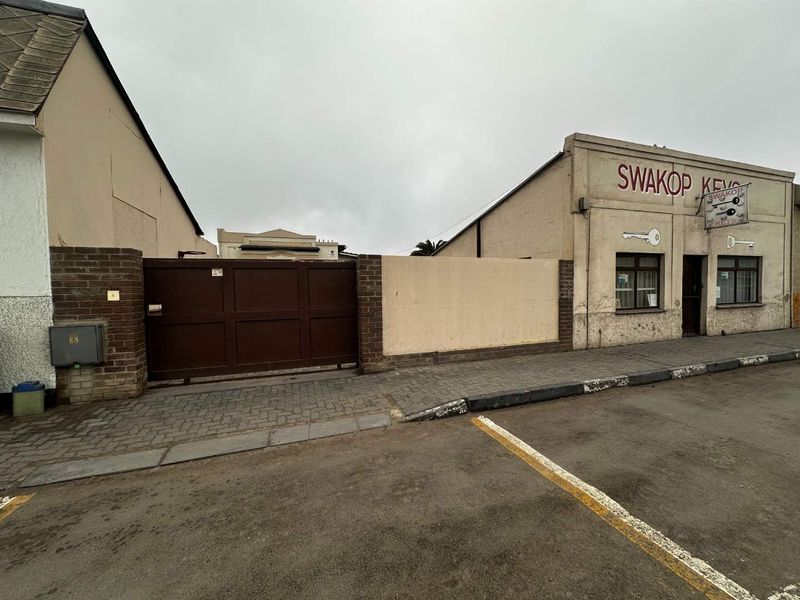 Street-facing view of a commercial property featuring a brick boundary wall, metal gate, and signage for a key cutting business.