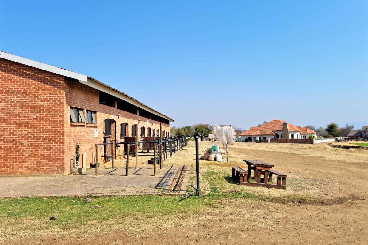 A view of a brick stable block with individual stalls, set on a large residential plot with surrounding landscape.