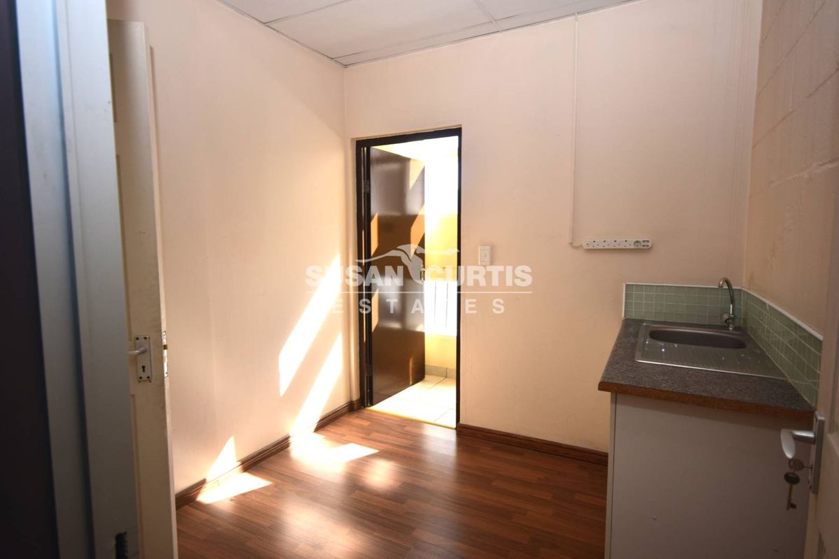 A compact kitchenette area featuring a single sink, laminate countertop, tiled backsplash, and wood-look laminate flooring.