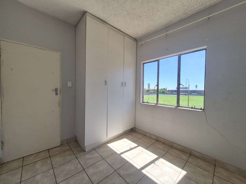 An empty bedroom featuring tiled flooring, a built-in wardrobe, and a window with views of the surrounding area.