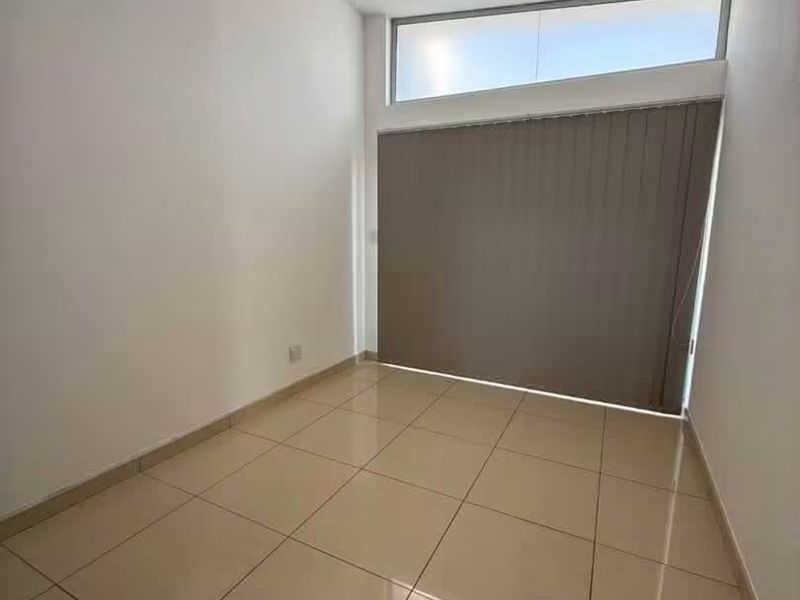 A bright, empty bedroom featuring neutral tiled flooring, a high-positioned clerestory window, and vertical blinds, offering a clean and versatile living space.