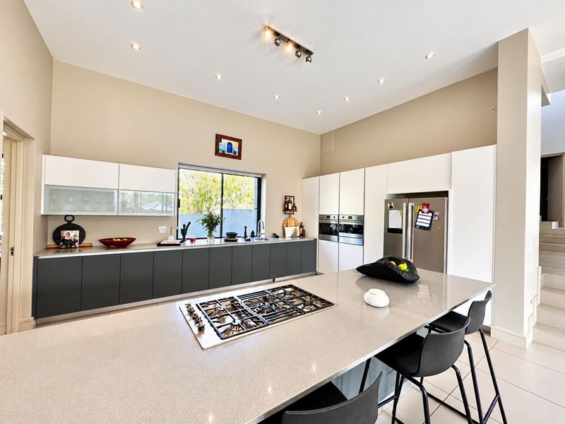 Modern kitchen featuring a large central island with a gas cooktop, sleek handleless cabinetry, stone countertops, and high-end built-in double ovens.