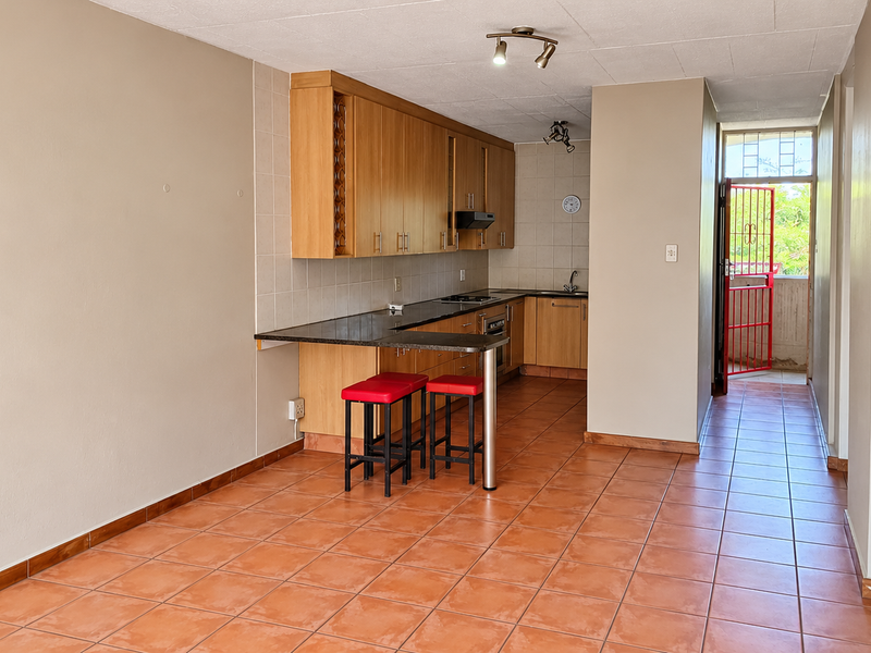 Open-plan kitchen featuring wooden cabinetry, granite countertops, and tiled flooring, leading to a rear exit with a security gate.