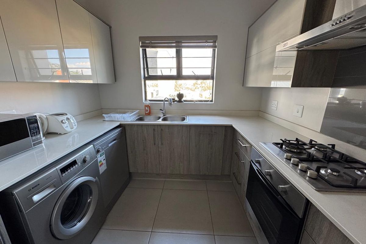 Modern kitchen featuring sleek cabinetry, stone countertops, integrated gas hob, oven, extractor fan, and tiled flooring with a functional layout.