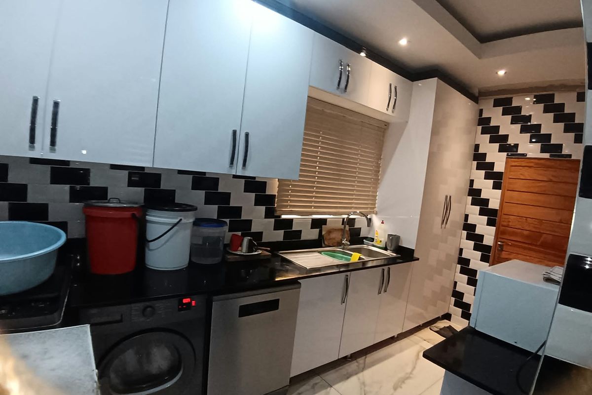 Modern kitchen featuring high-gloss white cabinetry, black granite countertops, integrated appliances, and a distinctive black and white tiled splashback.