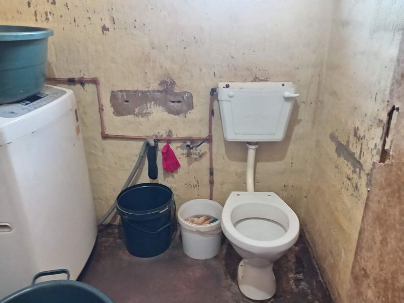 A utility space featuring a toilet and exposed plumbing, currently in need of significant maintenance and cosmetic renovation to improve its condition.