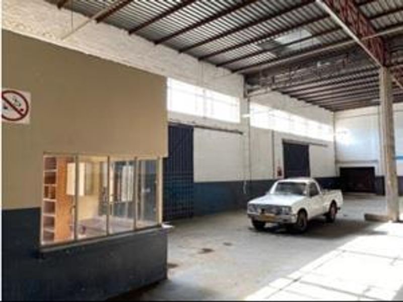Spacious industrial warehouse area featuring high ceilings with exposed steel trusses, concrete flooring, and an integrated internal office partition.