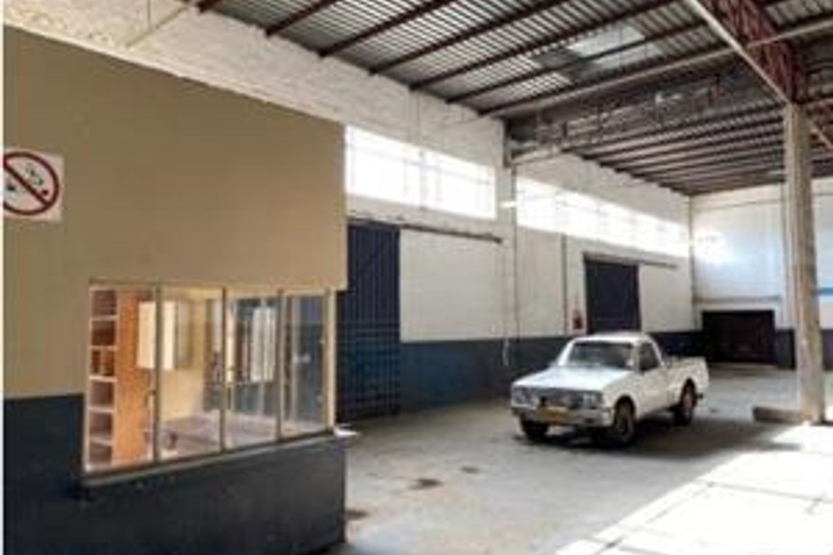 Spacious industrial warehouse area featuring high ceilings with exposed steel trusses, concrete flooring, and an integrated internal office partition.