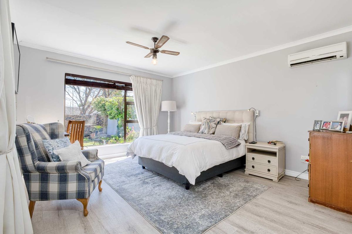 A well-maintained bedroom featuring light wood-look flooring, a ceiling fan, and a wall-mounted air conditioning unit with views of the garden.