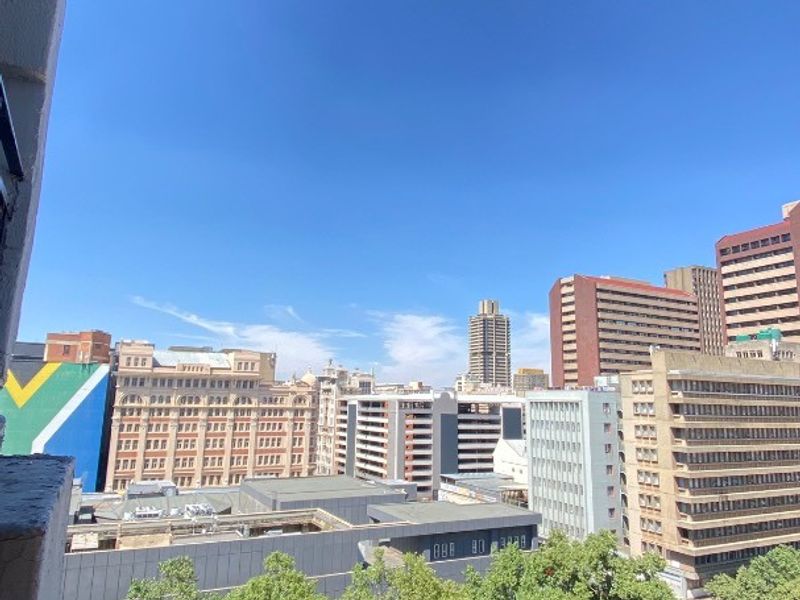 An elevated urban cityscape view overlooking surrounding buildings and street-level greenery from an apartment balcony.