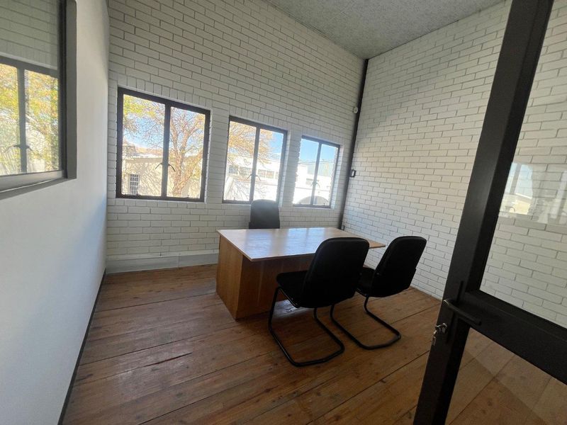 A functional office space featuring exposed white brick walls, natural timber flooring, and large windows providing ample natural light.