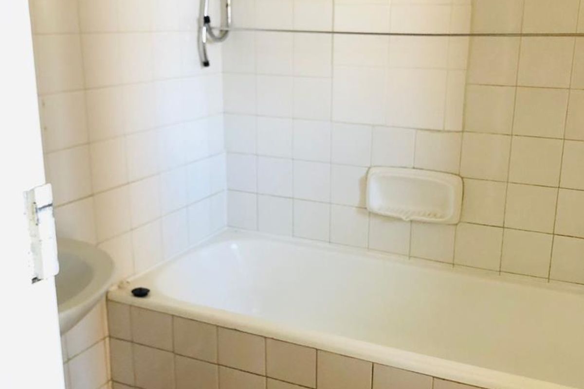 A dated bathroom featuring a standard bathtub, wall tiling, and a basic washbasin, requiring modernization to improve its overall condition and appeal.