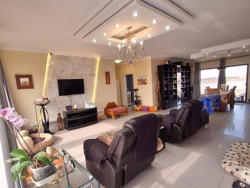 Spacious open-plan living area featuring a stone accent wall, recessed ceiling with integrated lighting, and large sliding doors leading to an outdoor space.