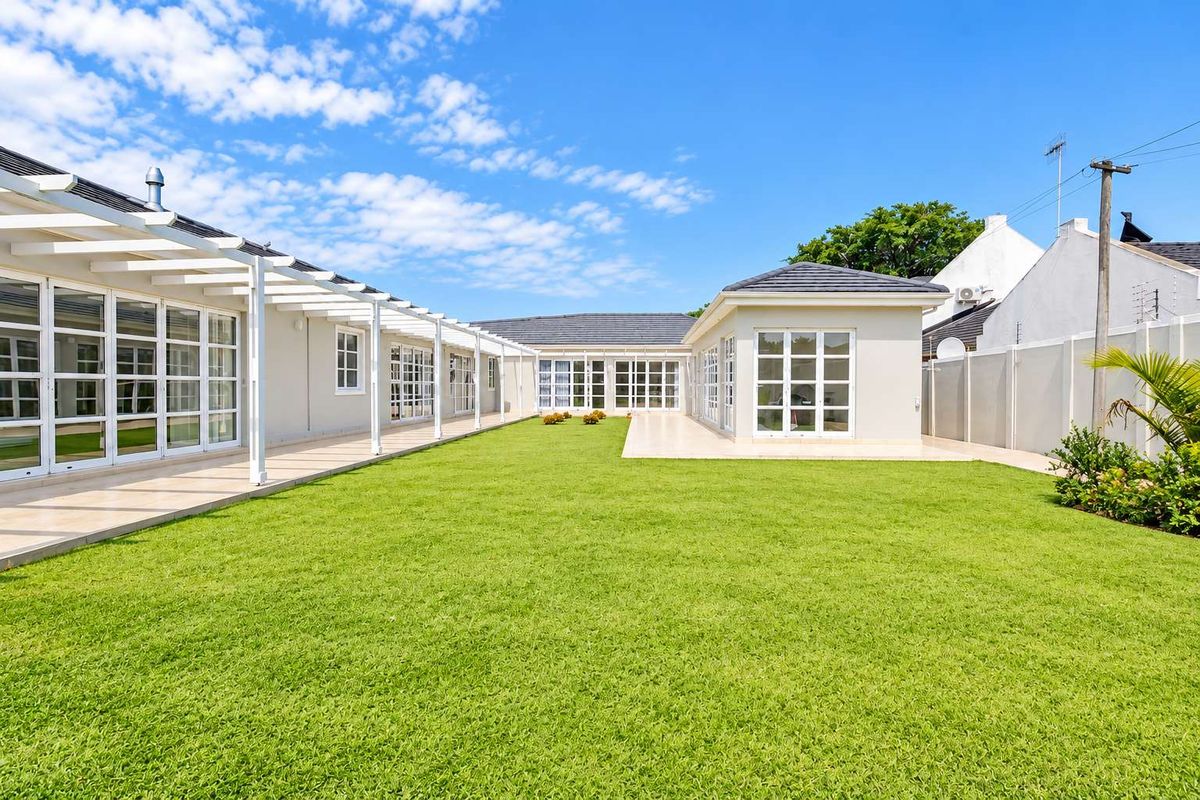 Spacious rear garden featuring a well-maintained lawn, extensive tiled patio area, and a covered pergola extending along the house facade.