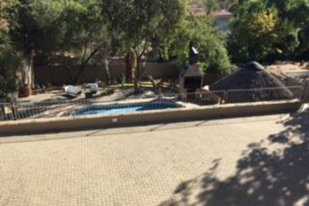 Elevated view of a backyard featuring a swimming pool, paved patio area, built-in braai, and a thatched lapa structure.