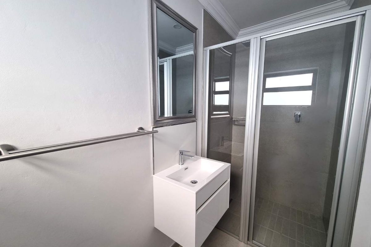 A modern, clean bathroom featuring a wall-mounted vanity, basin, and a glass-enclosed shower with neutral tiling.