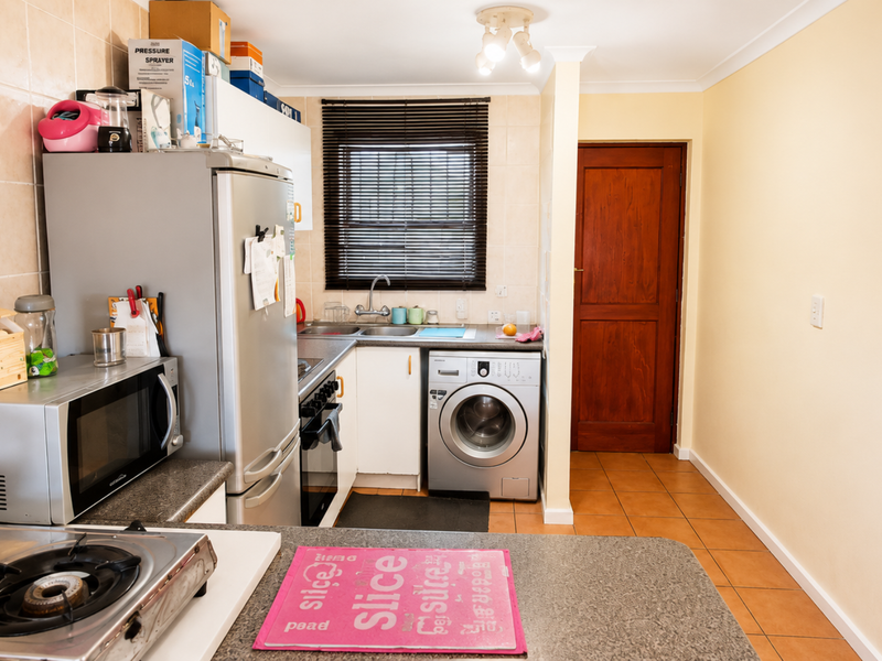 A functional kitchen featuring tiled splashbacks, laminate countertops, built-in cabinetry, and integrated laundry appliance space.