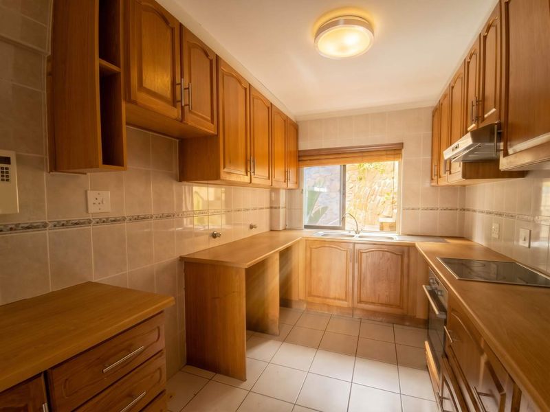 A functional kitchen featuring wooden cabinetry, laminate countertops, a double basin sink, and built-in appliances including an oven and electric hob.