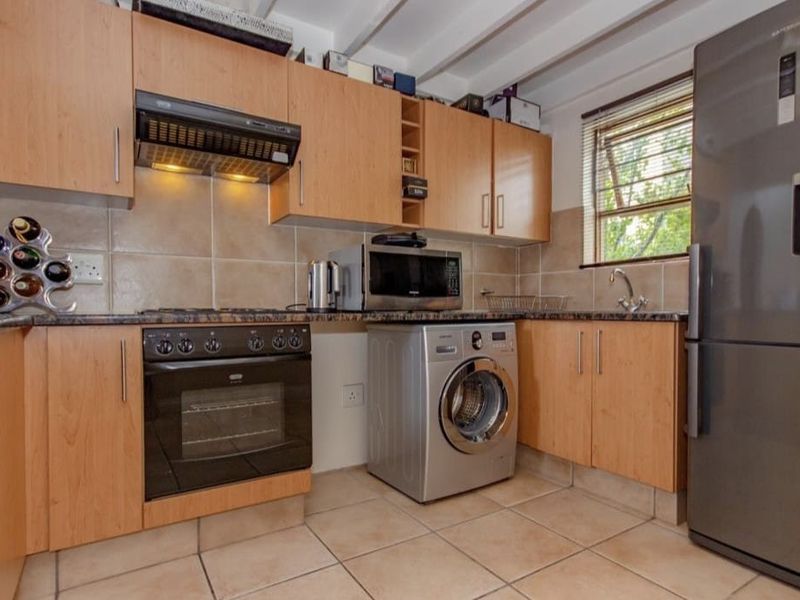 Functional kitchen featuring laminate cabinetry, granite countertops, built-in oven, extractor fan, tiled backsplash, and tiled flooring with exposed ceiling beams.