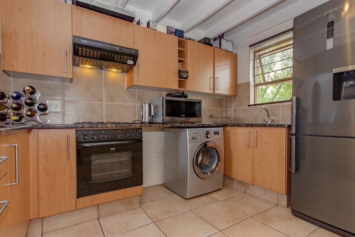 Functional kitchen featuring laminate cabinetry, granite countertops, built-in oven, extractor fan, tiled backsplash, and tiled flooring with exposed ceiling beams.