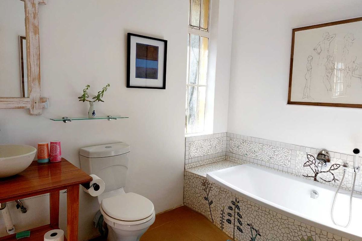 A bathroom featuring a built-in bathtub with decorative mosaic tiling, a pedestal-style vanity, and a standard toilet.