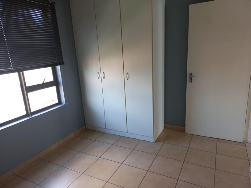 A clean, empty bedroom featuring tiled flooring, a built-in wardrobe, and a window fitted with a venetian blind.