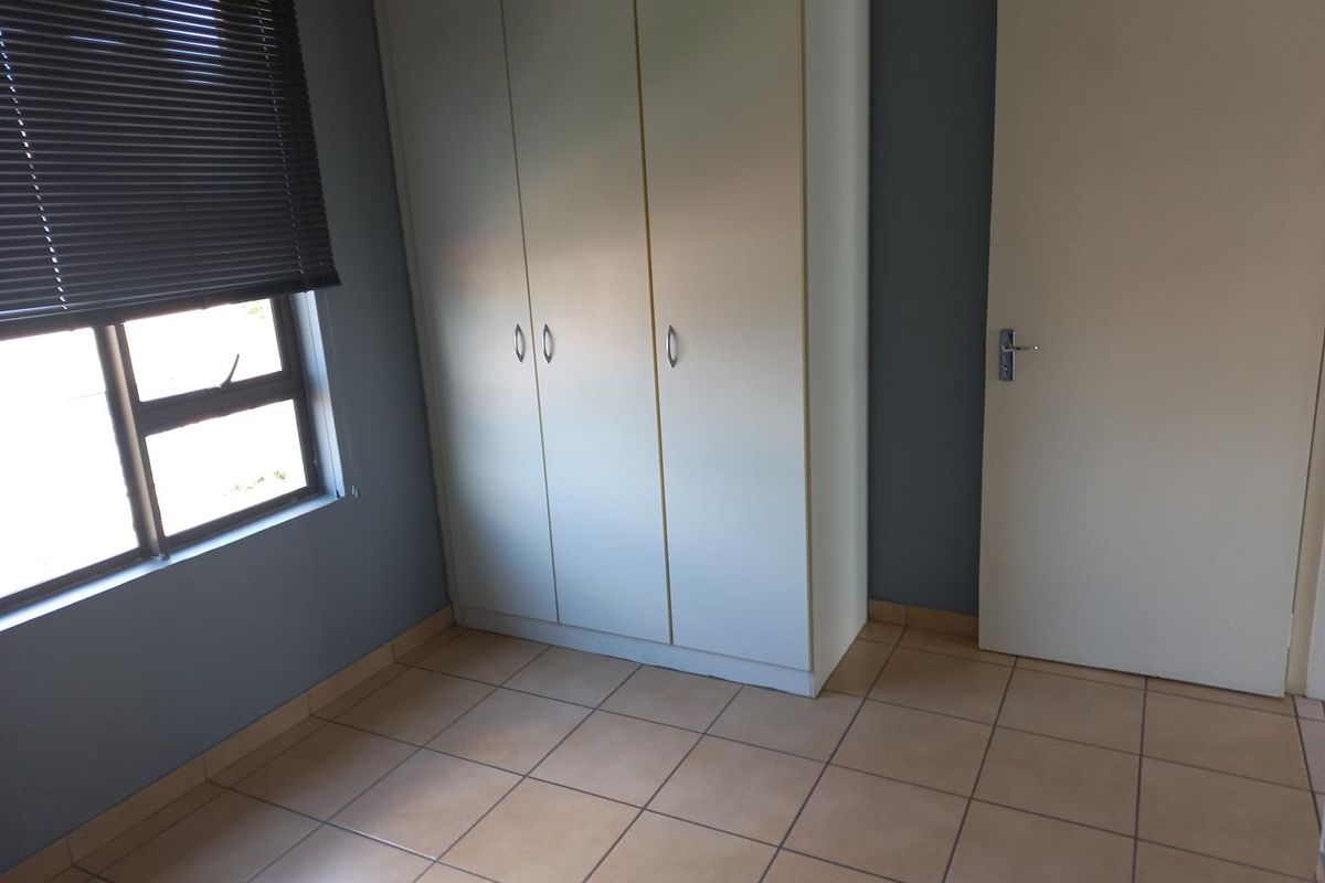 A clean, empty bedroom featuring tiled flooring, a built-in wardrobe, and a window fitted with a venetian blind.