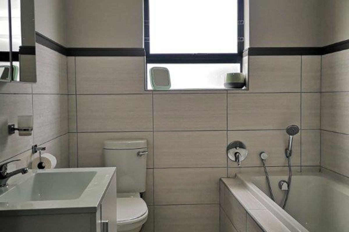 A modern, well-maintained bathroom featuring a vanity cabinet, toilet, and a bathtub with a shower mixer, finished with neutral wall and floor tiles.