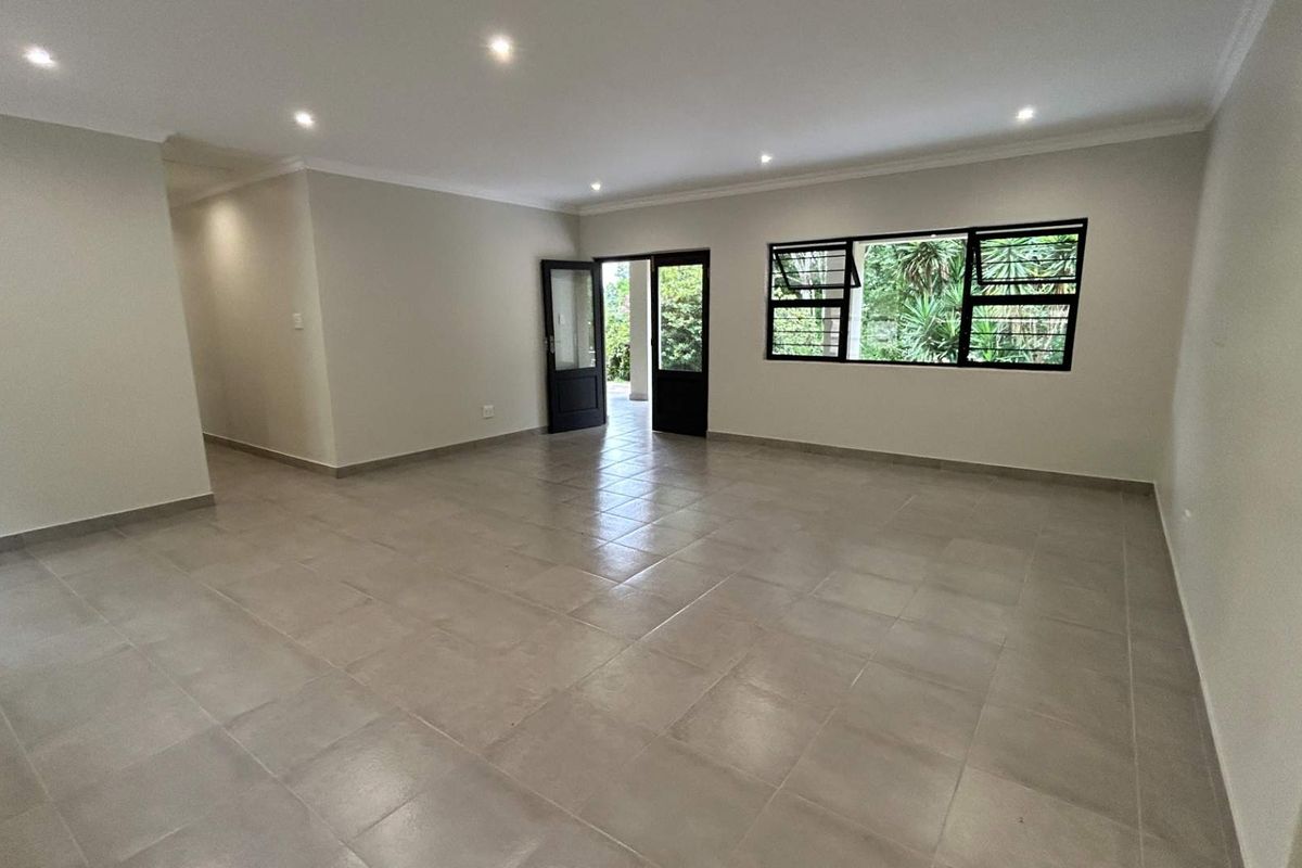 A spacious, empty living area featuring neutral tiled flooring, recessed downlighting, and black-framed windows and doors leading to the exterior.
