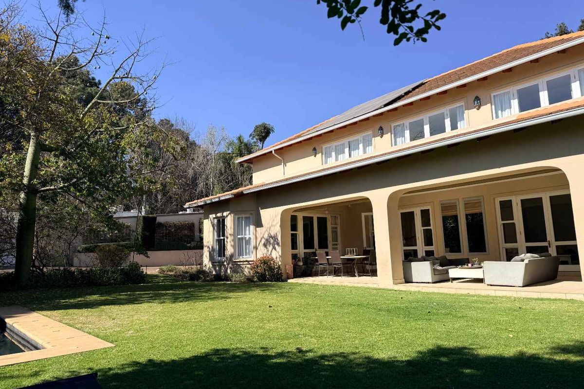Rear view of the property featuring a spacious covered patio, well-maintained lawn, and a swimming pool set within a landscaped garden.