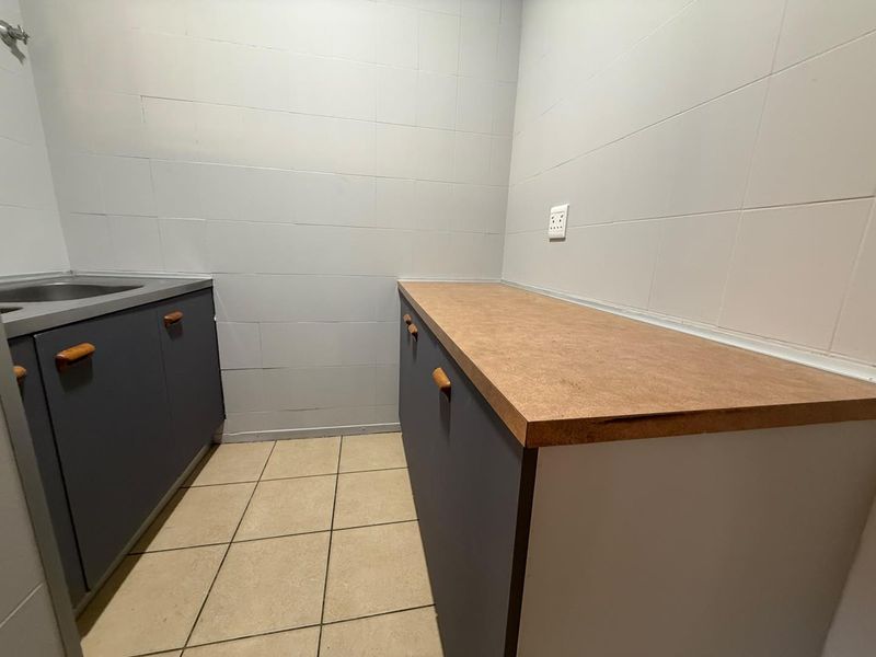 A functional laundry area featuring built-in cabinetry, a laminate countertop, and a stainless steel sink with tiled walls and flooring.
