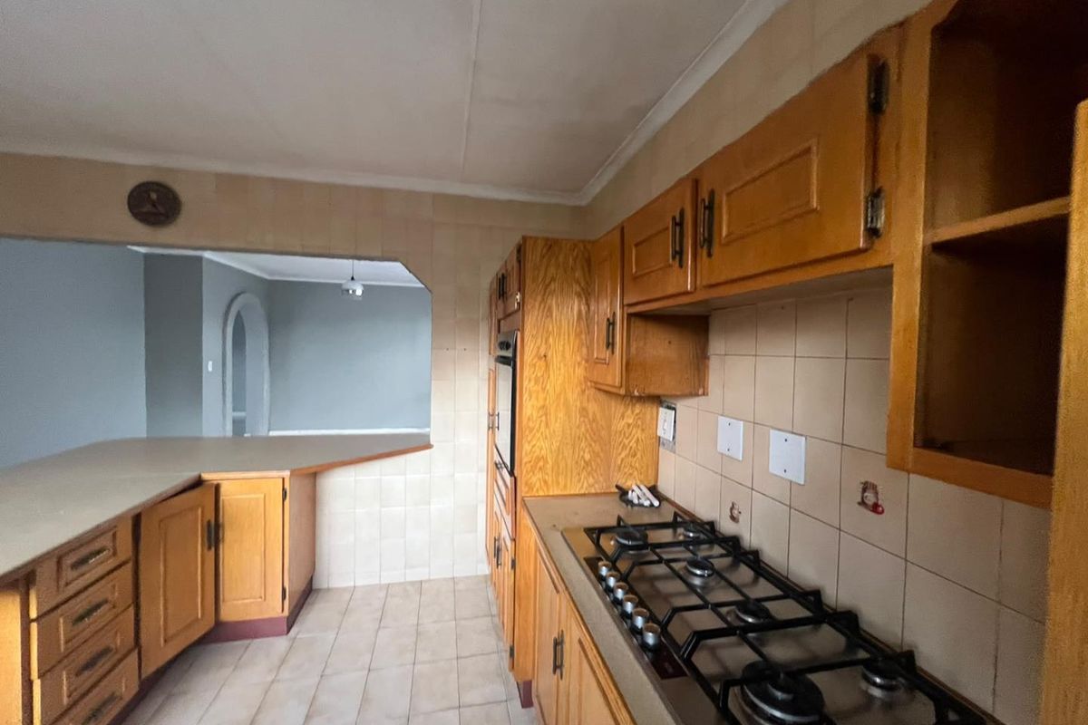 A dated kitchen featuring wooden cabinetry, a gas hob, built-in oven, and a convenient pass-through window connecting to the adjacent living area.