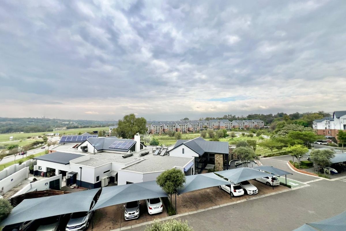 An elevated aerial view of the apartment complex grounds, featuring paved parking areas with shade structures, solar panel installations, and surrounding landscaped estate views.