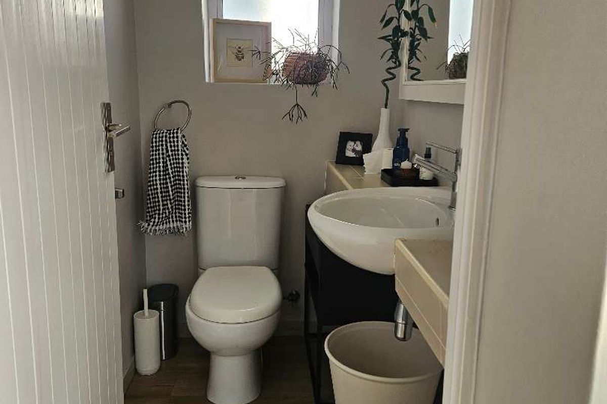 A compact, well-maintained bathroom featuring a modern washbasin, toilet, and wood-look laminate flooring with natural light from a frosted window.