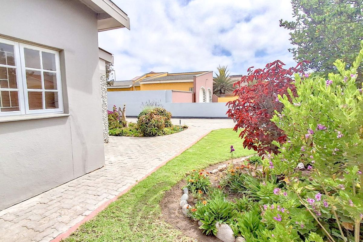 A well-maintained rear garden area featuring paved walkways, manicured lawn, and established garden beds alongside the side elevation of the house.