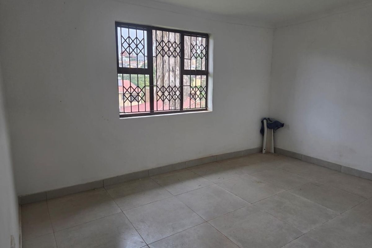 An empty bedroom featuring tiled flooring and a window fitted with a security gate, offering a blank canvas for potential interior design.