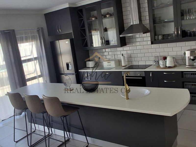 Modern kitchen featuring dark cabinetry, stone countertops, a central island with seating, and a subway tile backsplash.