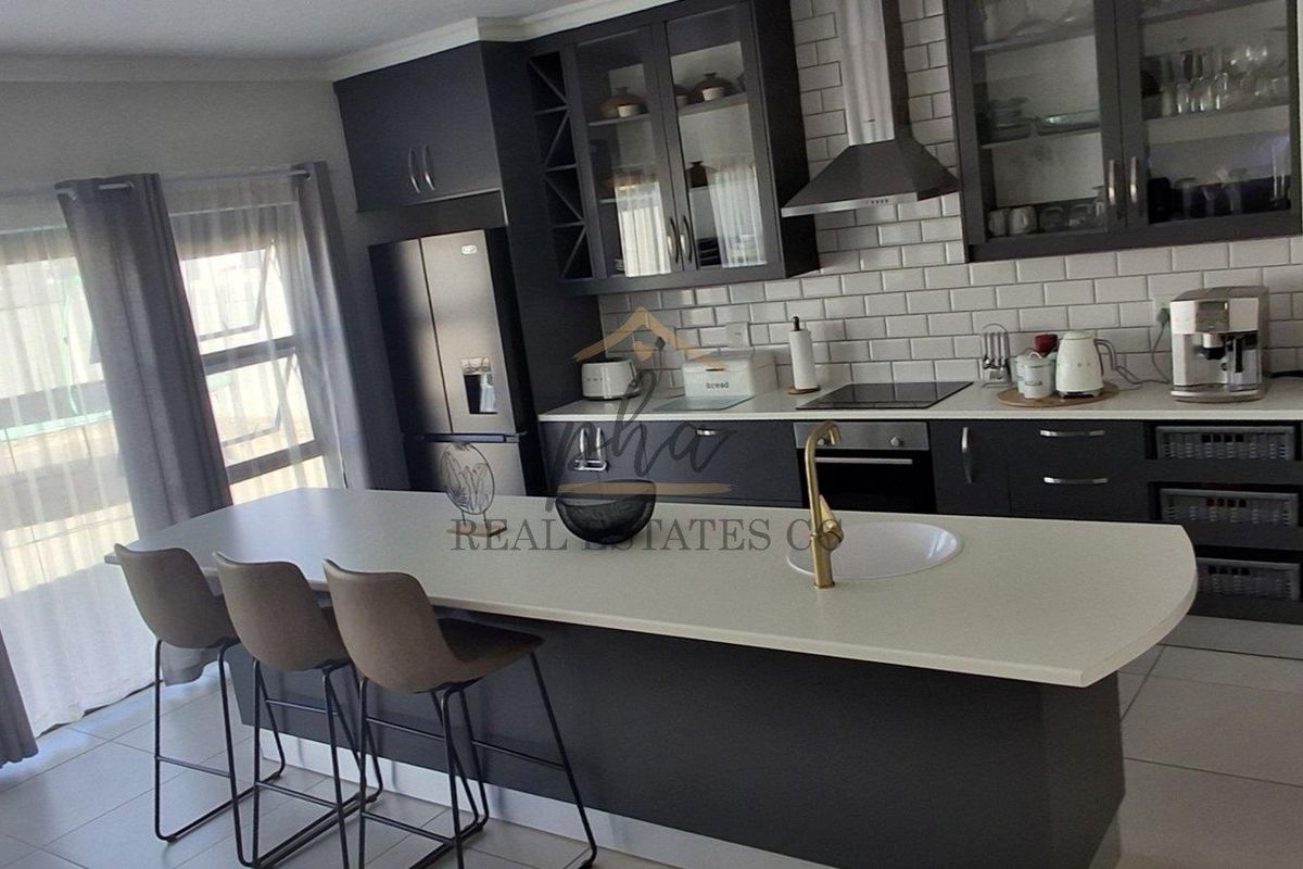 Modern kitchen featuring dark cabinetry, stone countertops, a central island with seating, and a subway tile backsplash.