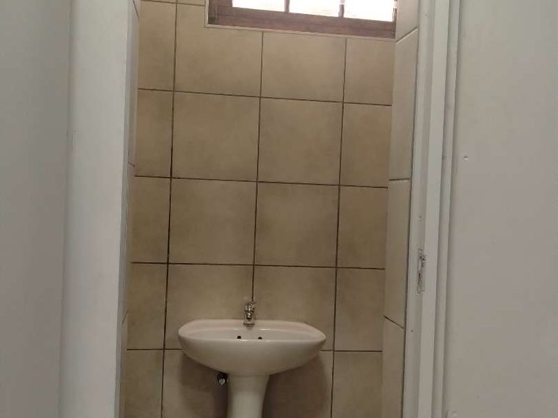 A small, functional bathroom featuring a pedestal basin, tiled walls, and tiled flooring with a small window for ventilation.