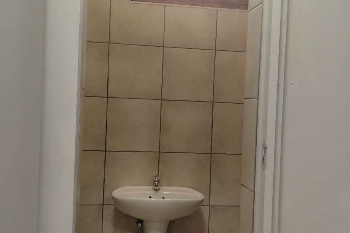 A small, functional bathroom featuring a pedestal basin, tiled walls, and tiled flooring with a small window for ventilation.