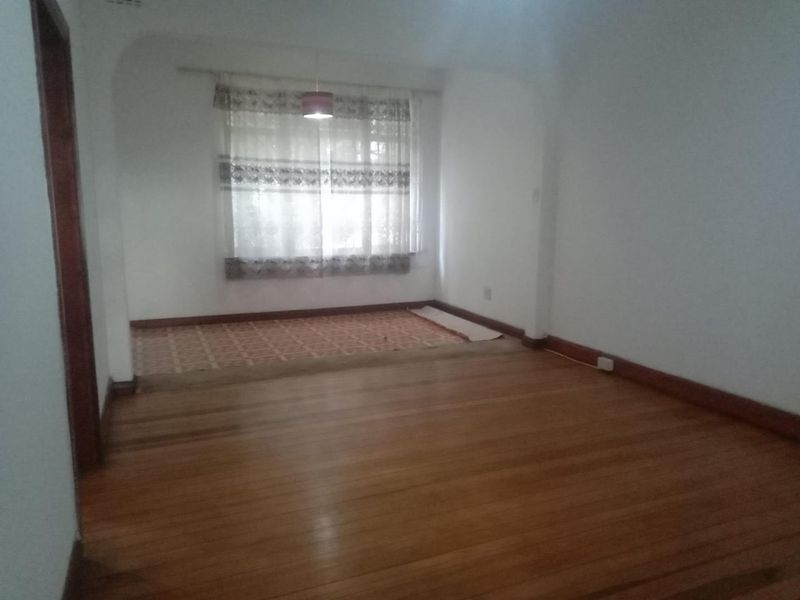 An empty living room featuring hardwood flooring, a raised tiled area, and an arched transition, offering a blank canvas for renovation.